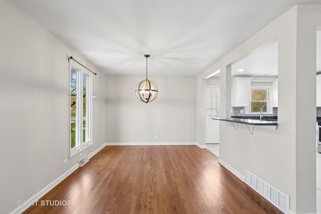 unfurnished dining area featuring wood finished floors, visible vents, a healthy amount of sunlight, and baseboards