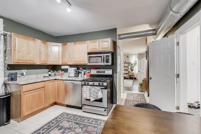 kitchen with light tile patterned flooring, appliances with stainless steel finishes, light stone counters, and light brown cabinets
