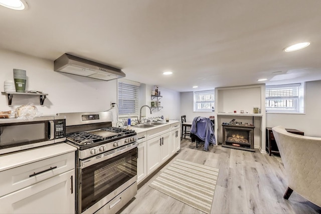 kitchen featuring a sink, white cabinetry, extractor fan, light wood-style floors, and appliances with stainless steel finishes