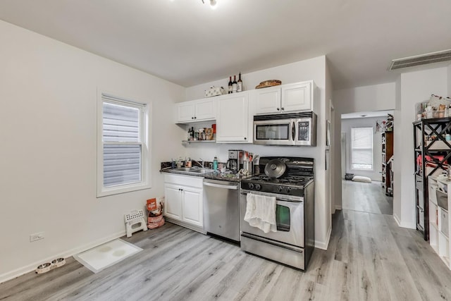 kitchen with stainless steel appliances, white cabinetry, and light wood-style flooring