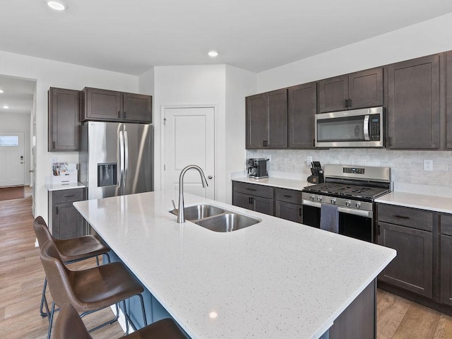 kitchen with a kitchen breakfast bar, tasteful backsplash, a sink, dark brown cabinetry, and stainless steel appliances