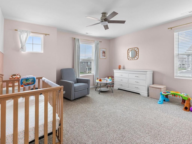 bedroom with carpet, visible vents, a crib, and ceiling fan