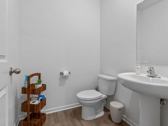 bathroom featuring baseboards, wood finished floors, a sink, and toilet