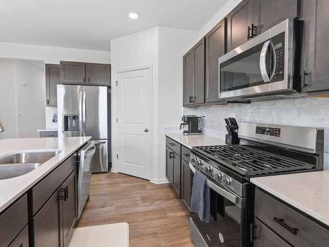 kitchen with a sink, light wood-type flooring, dark brown cabinetry, appliances with stainless steel finishes, and recessed lighting