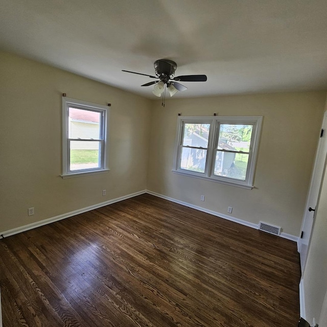 empty room featuring healthy amount of natural light, dark wood-style floors, ceiling fan, and baseboards