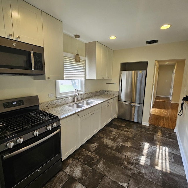 kitchen with appliances with stainless steel finishes, a sink, white cabinetry, light stone counters, and baseboards