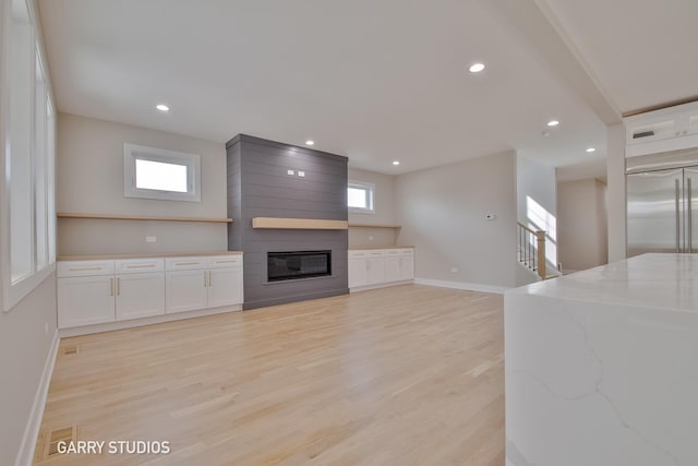 unfurnished living room with a fireplace, light wood-type flooring, a healthy amount of sunlight, and baseboards