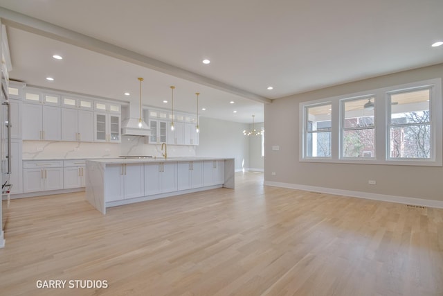 kitchen featuring light countertops, a large island with sink, custom exhaust hood, and white cabinetry