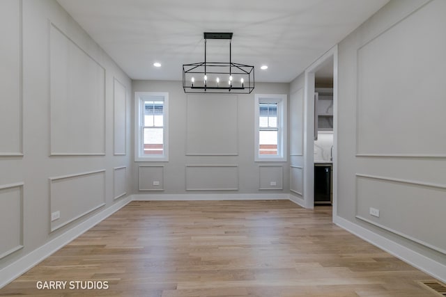 unfurnished dining area with light wood finished floors, visible vents, a notable chandelier, and a decorative wall