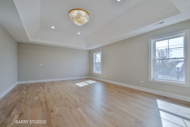 unfurnished room with baseboards, light wood-style floors, and a raised ceiling