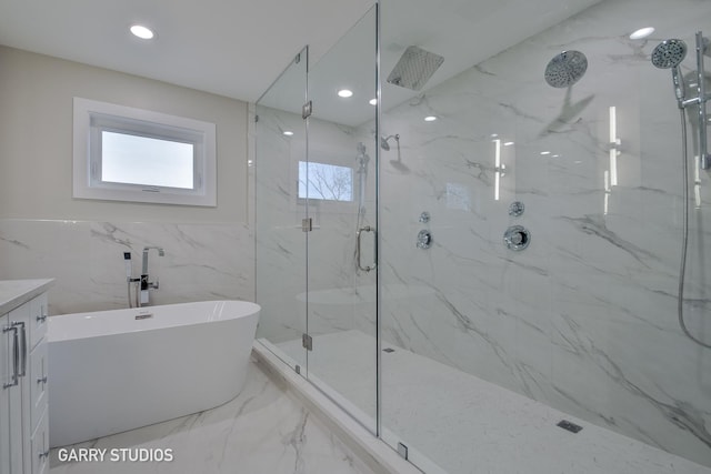 bathroom with a freestanding bath, vanity, a marble finish shower, and tile walls