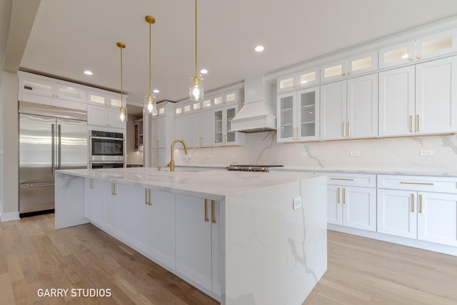 kitchen with light wood-type flooring, stainless steel appliances, a sink, and custom range hood