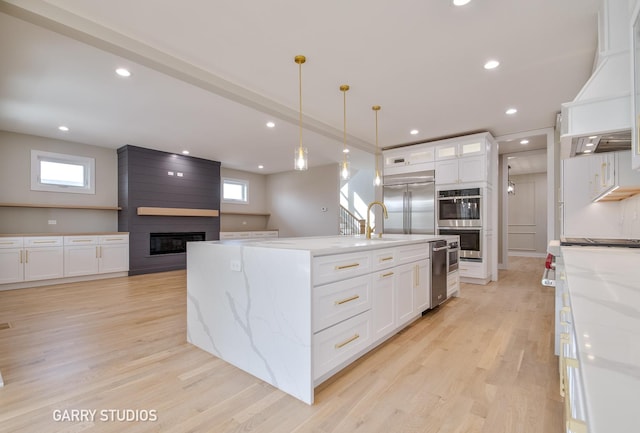kitchen with light wood finished floors, stainless steel appliances, a sink, white cabinetry, and a large fireplace