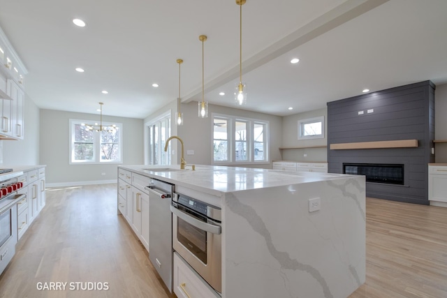 kitchen featuring a large fireplace, stainless steel appliances, a sink, and light wood-style flooring