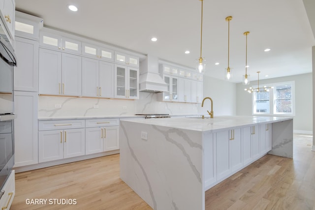 kitchen with light wood-type flooring, a sink, white cabinetry, and premium range hood