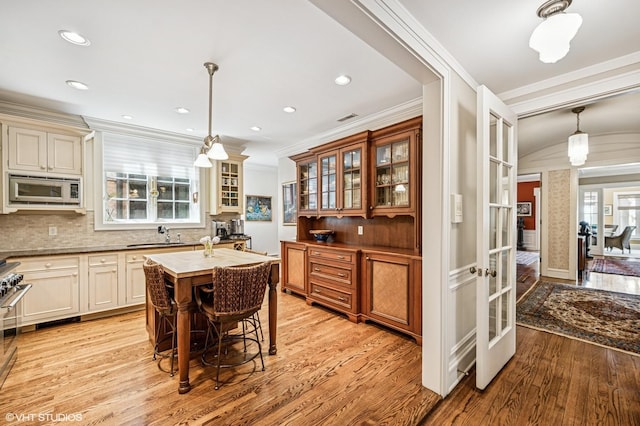kitchen featuring backsplash, crown molding, light wood finished floors, and stainless steel microwave