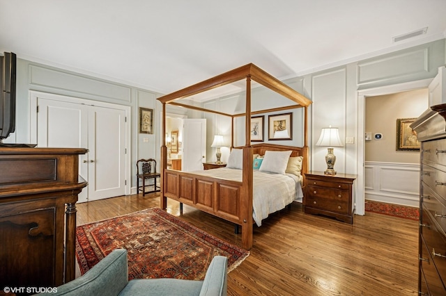 bedroom with visible vents, wood finished floors, and a decorative wall