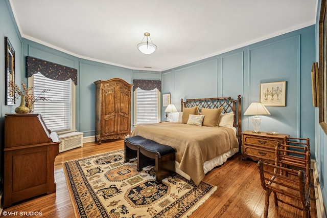 bedroom featuring ornamental molding, wood finished floors, multiple windows, and a decorative wall