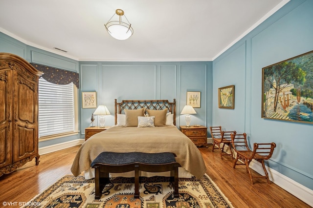 bedroom featuring baseboards, visible vents, wood finished floors, and a decorative wall