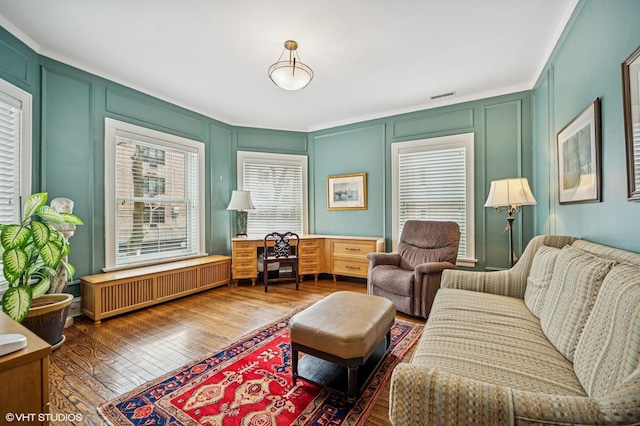 living room featuring visible vents, radiator heating unit, wood finished floors, and a decorative wall
