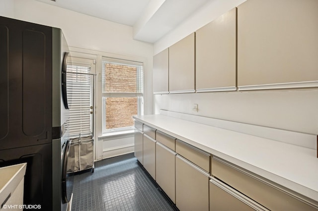 laundry room with stacked washing maching and dryer, cabinet space, and dark tile patterned flooring