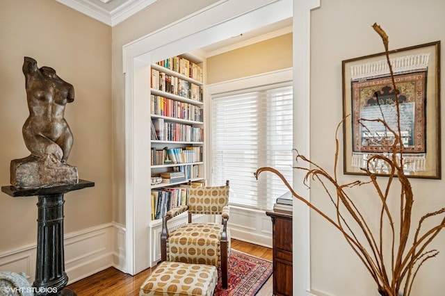 living area with a decorative wall, wood finished floors, a wainscoted wall, and ornamental molding