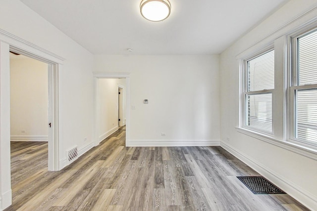 empty room featuring wood finished floors, visible vents, and baseboards