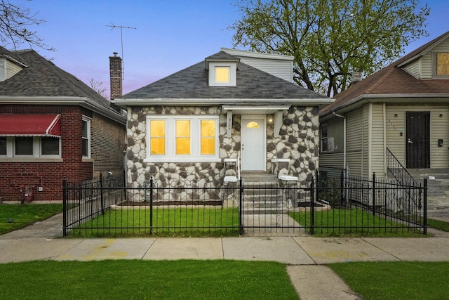 bungalow-style house featuring a yard, roof with shingles, a fenced front yard, and stone siding