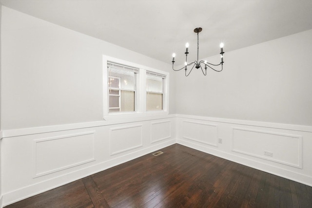 unfurnished dining area featuring dark wood-style floors, a chandelier, wainscoting, and visible vents
