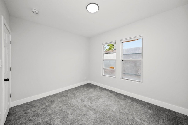 unfurnished room with dark carpet and baseboards