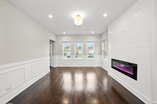 unfurnished living room featuring dark wood finished floors, a wainscoted wall, a glass covered fireplace, a decorative wall, and recessed lighting