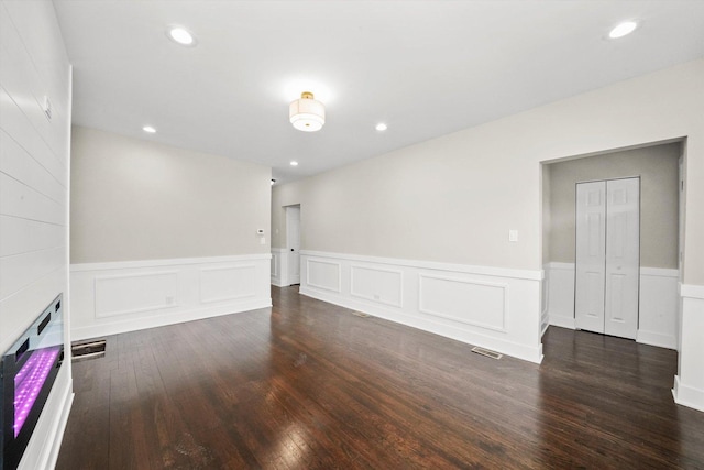 empty room featuring visible vents, dark wood finished floors, a wainscoted wall, a decorative wall, and recessed lighting