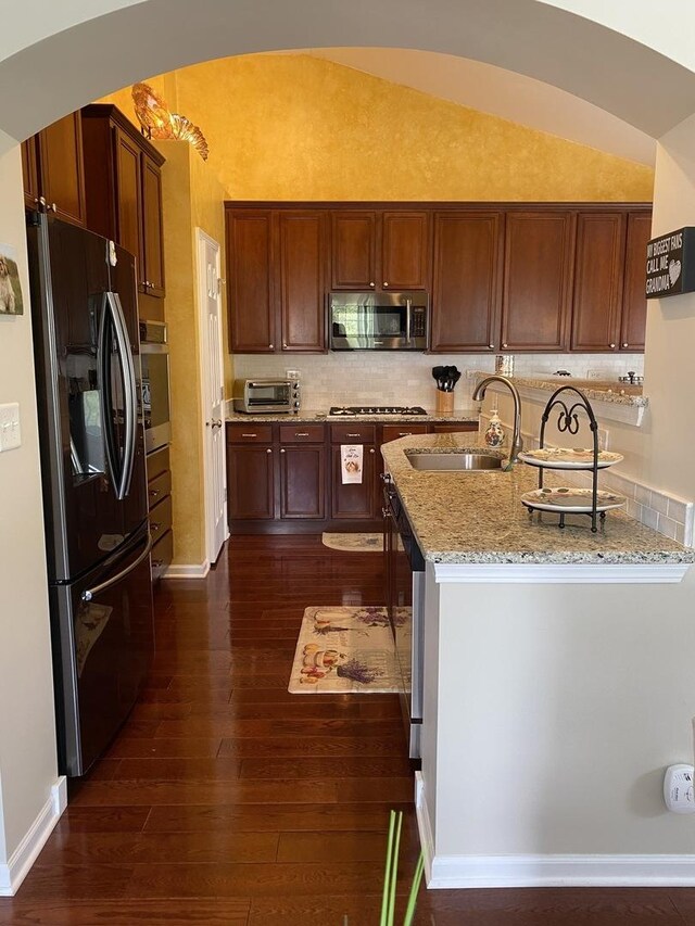 kitchen featuring dark wood finished floors, lofted ceiling, light stone counters, a sink, and appliances with stainless steel finishes