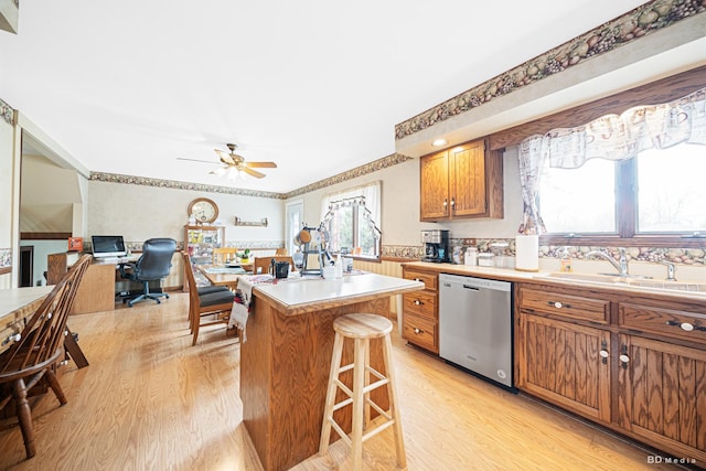 kitchen featuring a sink, light wood finished floors, dishwasher, and a kitchen bar
