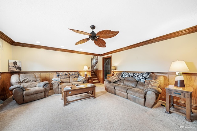 carpeted living room with crown molding, a ceiling fan, wooden walls, and a wainscoted wall