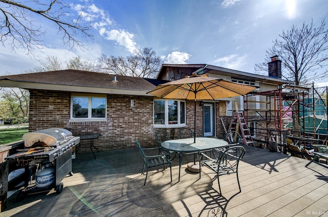 exterior space with a wooden deck, outdoor dining area, roof with shingles, a chimney, and brick siding