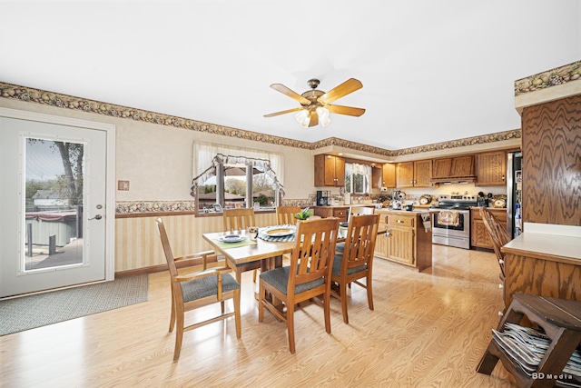 dining area featuring wainscoting, a ceiling fan, wallpapered walls, and light wood-style flooring