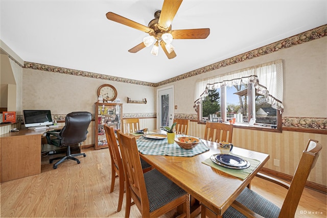 dining area featuring a wainscoted wall, ceiling fan, wallpapered walls, and light wood-style flooring
