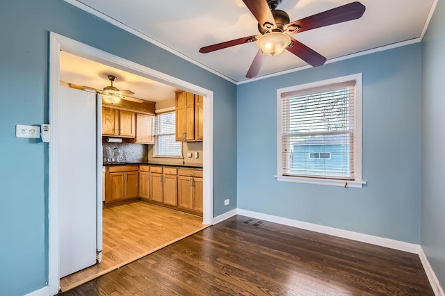 kitchen with dark countertops, wood finished floors, ceiling fan, and crown molding