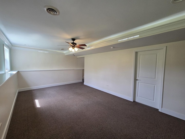 empty room with baseboards, visible vents, a ceiling fan, dark carpet, and crown molding