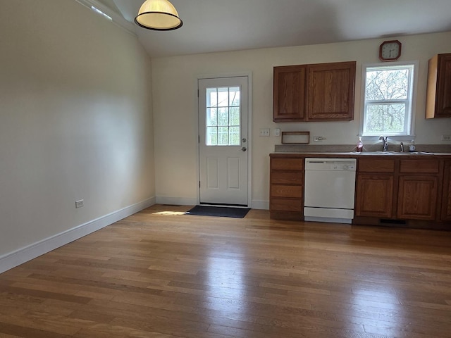 kitchen featuring white dishwasher, light wood-type flooring, brown cabinetry, and a sink