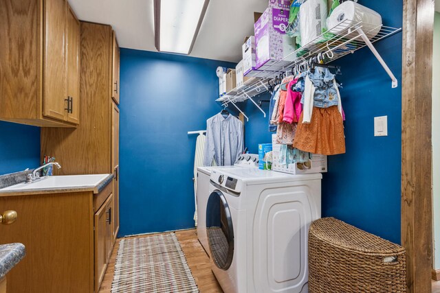 clothes washing area with a sink, light wood-style floors, cabinet space, and washer and dryer