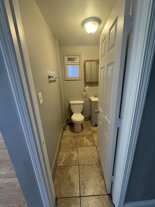 half bath featuring tile patterned flooring, baseboards, toilet, and vanity
