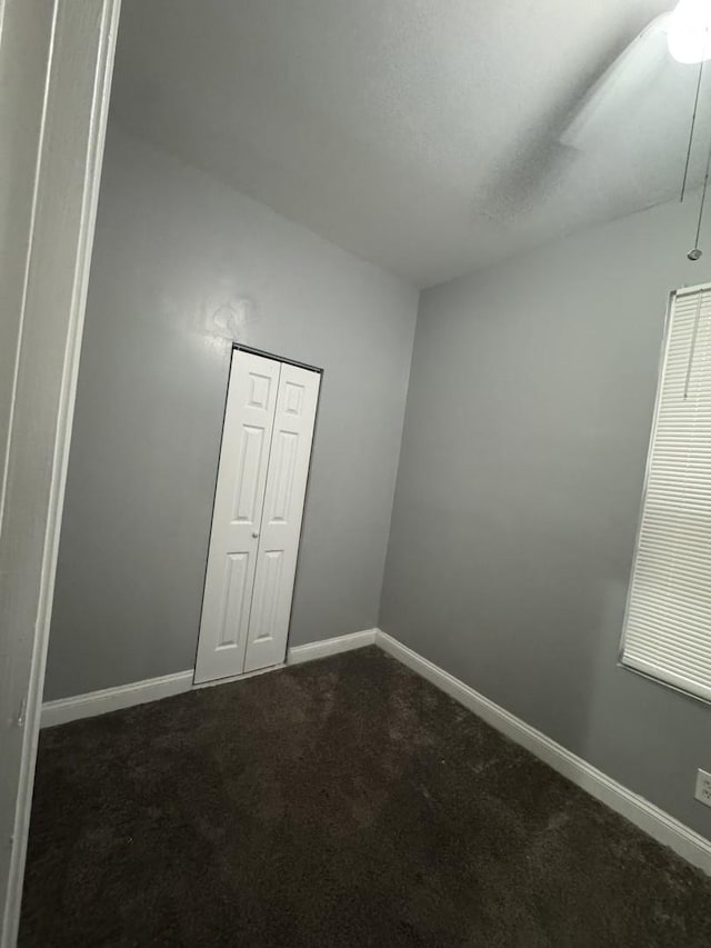 empty room featuring baseboards and dark colored carpet