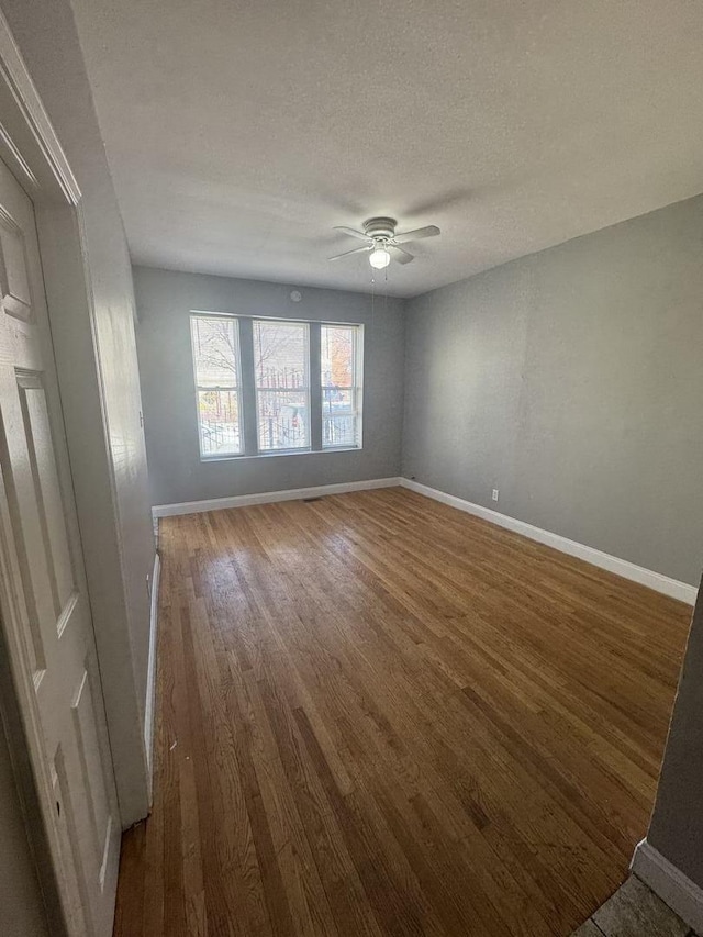 empty room with baseboards, wood finished floors, and ceiling fan