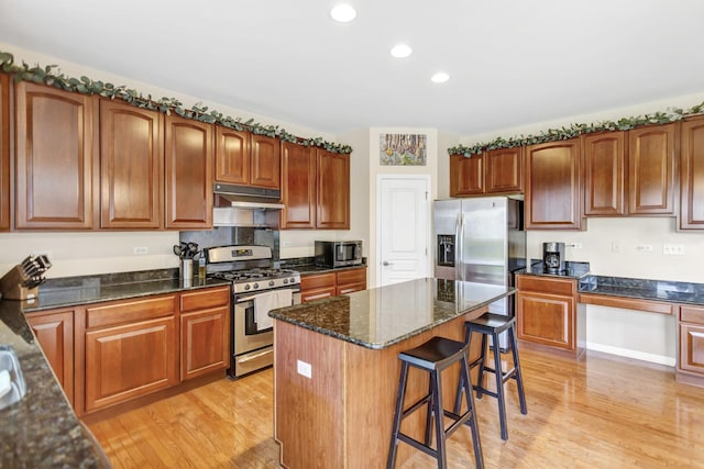 kitchen featuring a kitchen breakfast bar, under cabinet range hood, appliances with stainless steel finishes, and light wood-style flooring