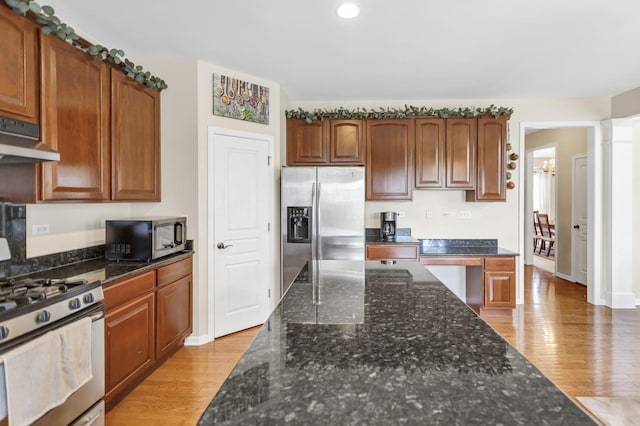 kitchen featuring light wood-style floors, dark stone countertops, stainless steel appliances, and under cabinet range hood