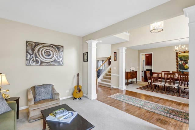 carpeted living area featuring stairway, an inviting chandelier, wood finished floors, baseboards, and decorative columns