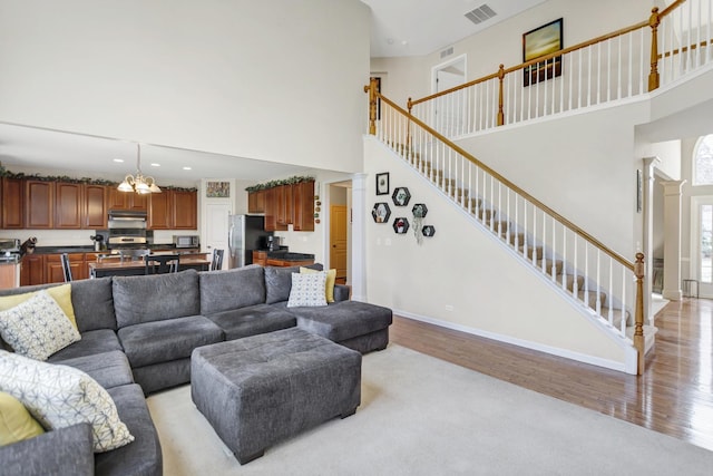 living room featuring light wood finished floors, visible vents, baseboards, a high ceiling, and stairway