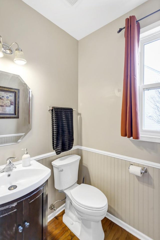 half bathroom featuring wainscoting, toilet, wood finished floors, and a wealth of natural light